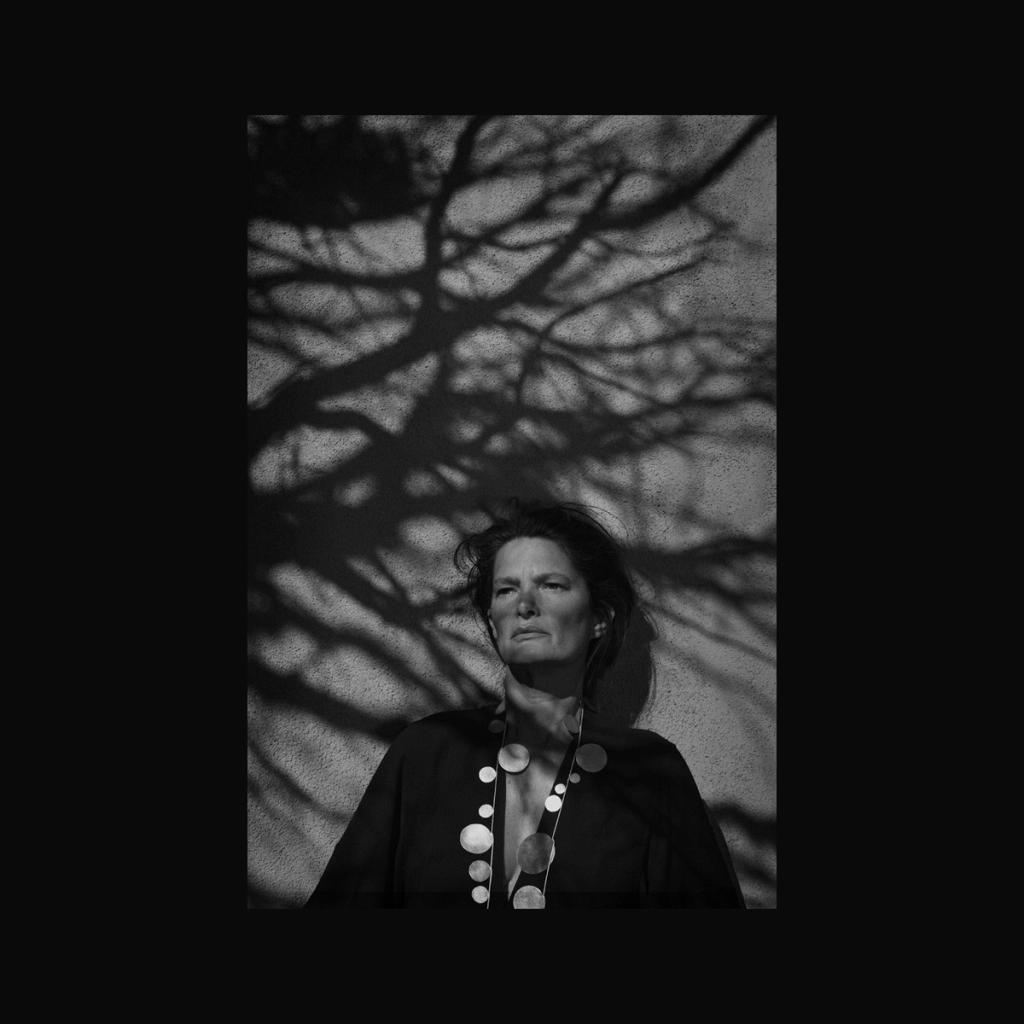 A woman in black against a wall with the shadow of bare tree branches