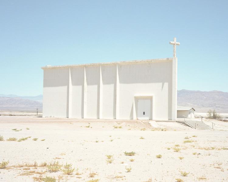A white church with a ribbed façade and a cross standing on a barren plain under a clear sky