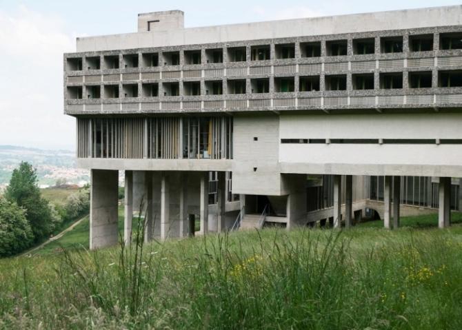 The concrete Couvent Sainte-Marie de La Tourette raised on pilotis on a green hillside