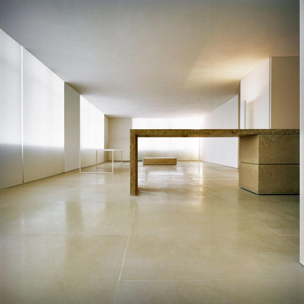 A light, bare hall with a stone bridging table and a slender white side table against the wall