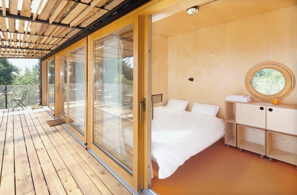 Спальня Containhotel с фанерными стенами, белой кроватью и выходом на деревянную террасу