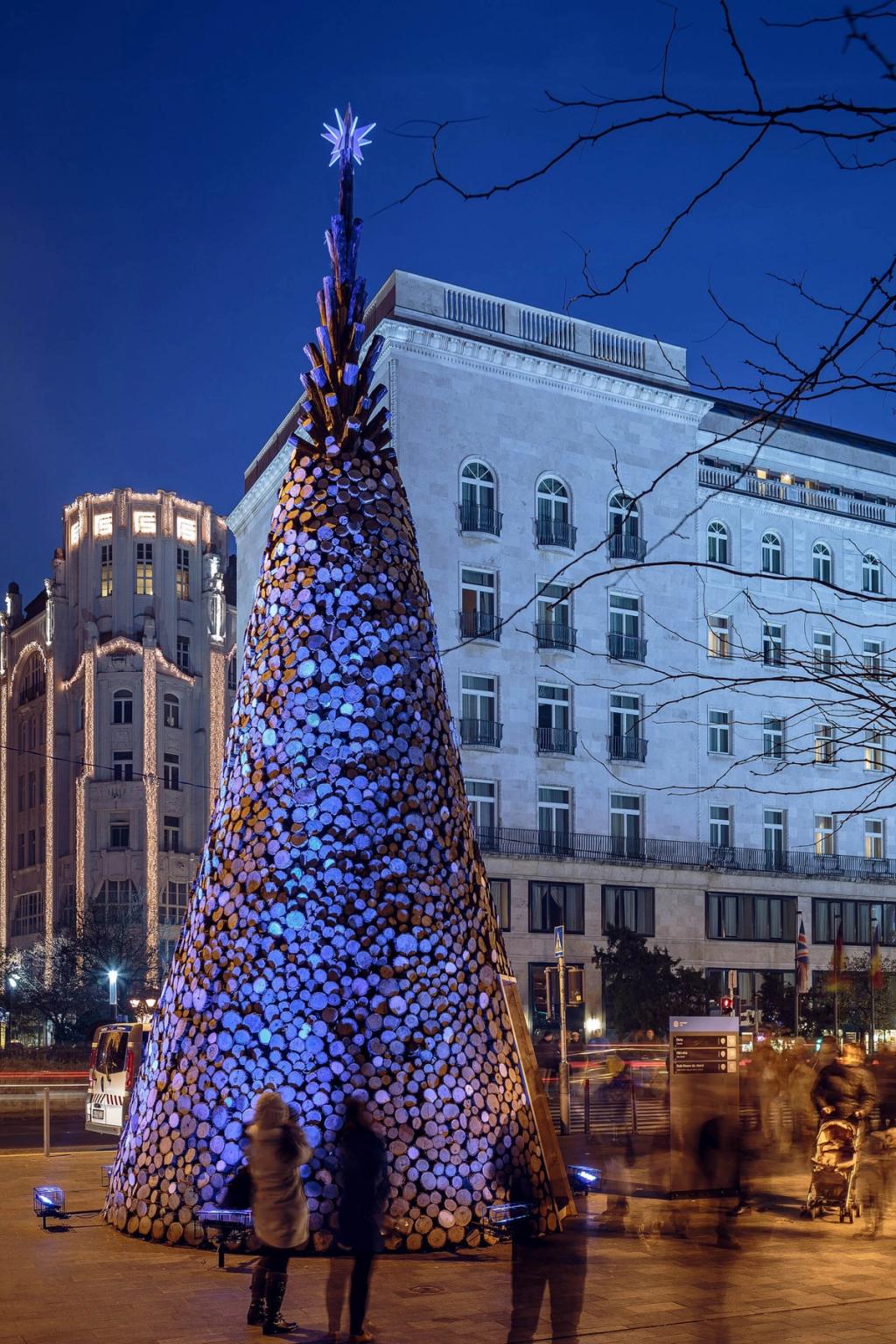 The same log tree illuminated in blue, with people gathered around it at dusk
