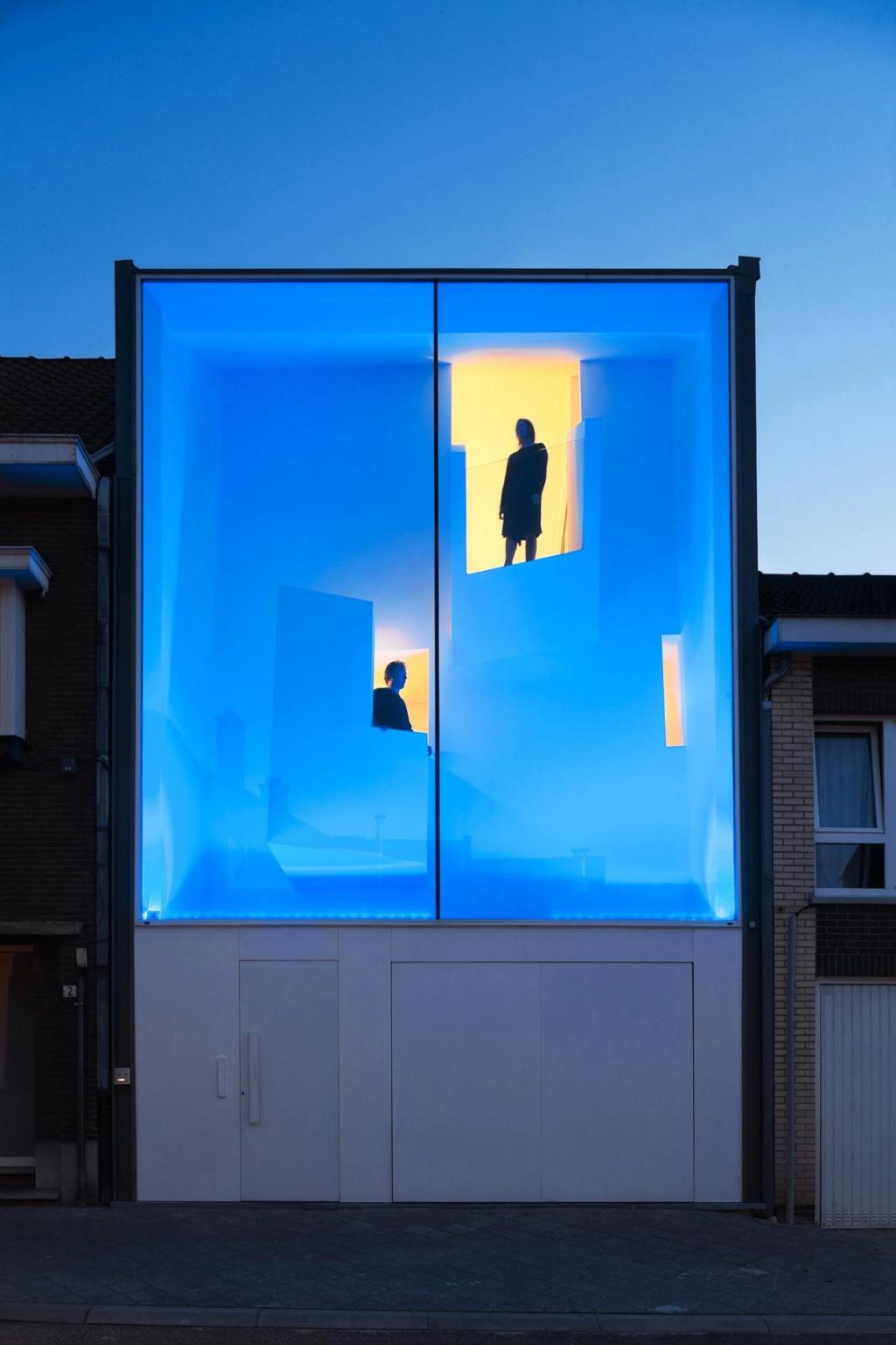 Узкий дом Narrow House в Билзене с синей подсветкой стеклянного фасада между кирпичными соседними домами