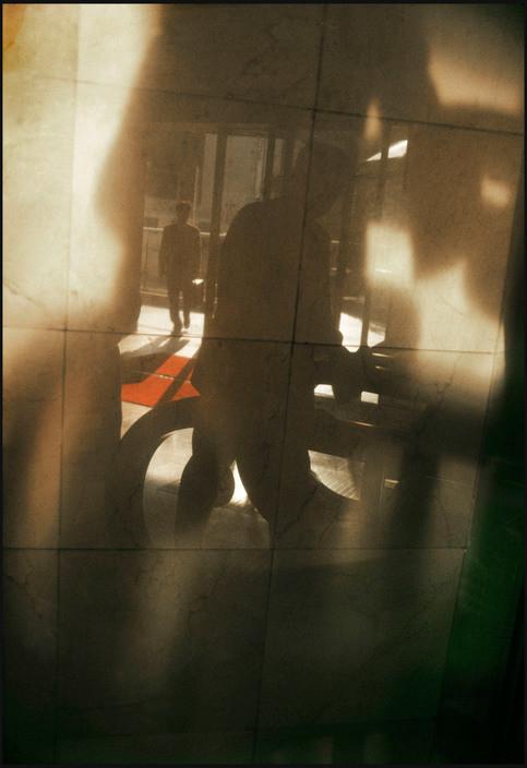 Blurred silhouettes of people in a lobby seen through glass, a red carpet and light reflections