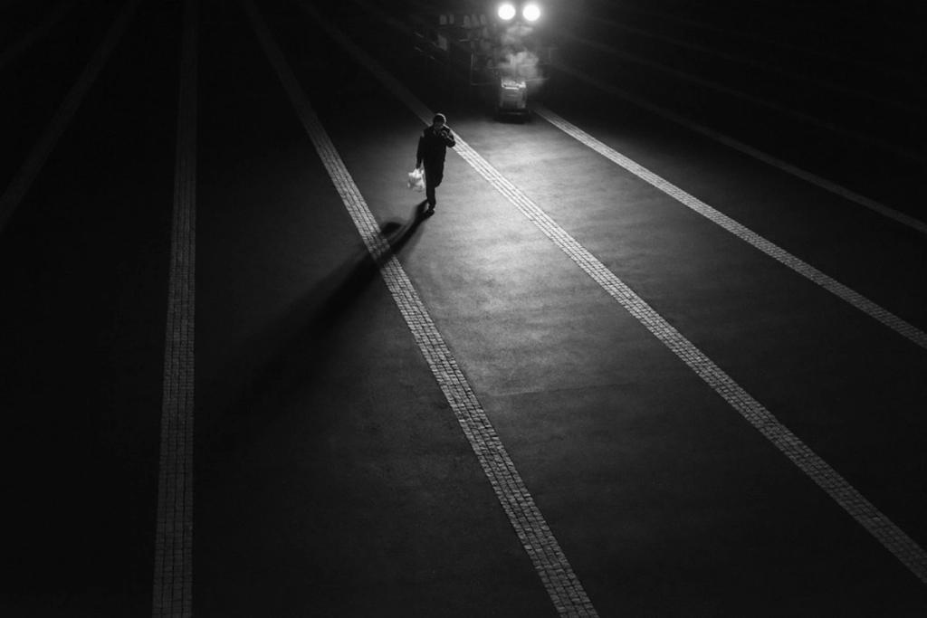 The silhouette of a person with a bag in a dark tunnel, headlights approaching from ahead