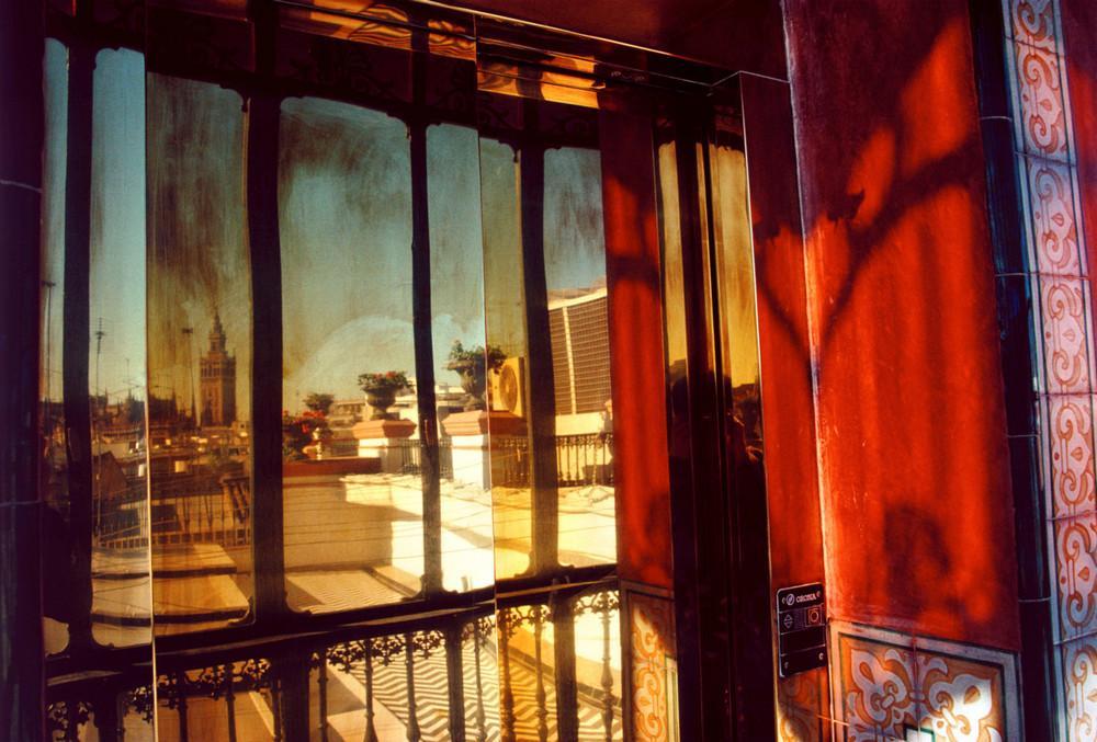 View from a window onto tiled rooftops and a tower in warm evening light, red walls