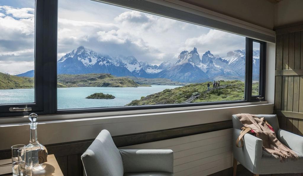 Armchairs by a panoramic window overlooking the turquoise lake and the peaks of Torres del Paine