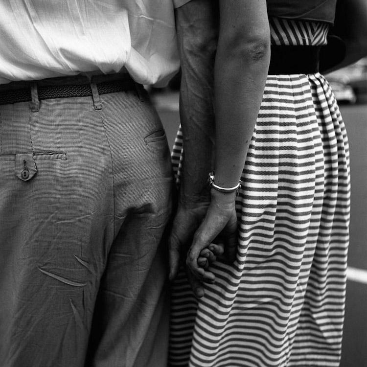 Black-and-white detail: the intertwined hands of a man and a woman in a striped skirt, seen from behind