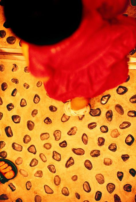 A child in a red dress seen from above on a floor with a pebble pattern, warm light