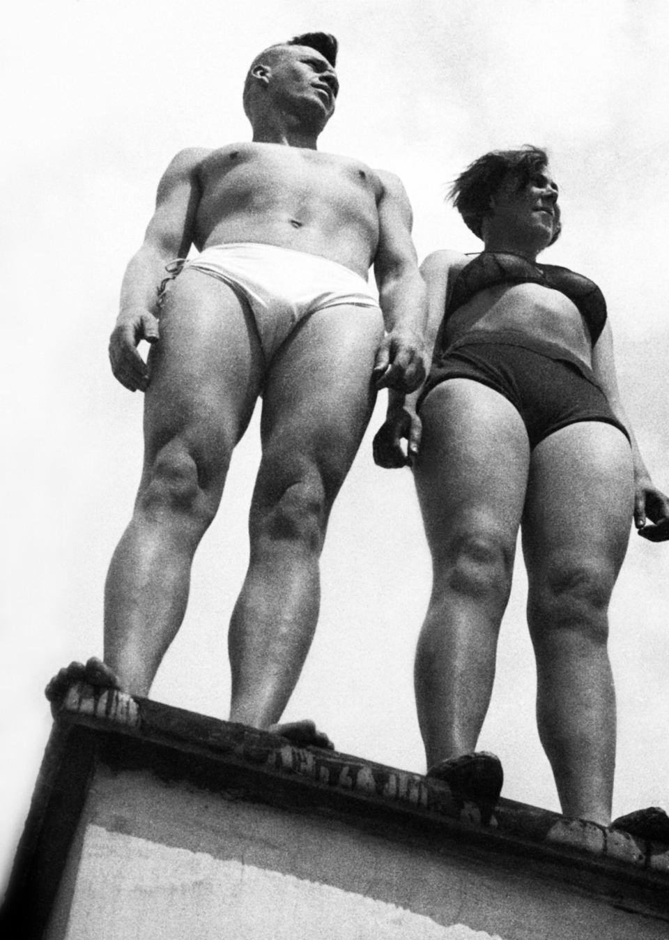 A male and female athlete in swimsuits on a diving platform, photographed from below