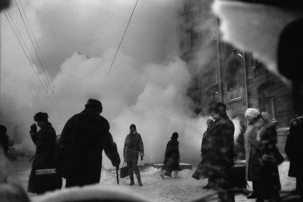 A black-and-white winter street, passers-by enveloped in a cloud of steam from a heating pipe