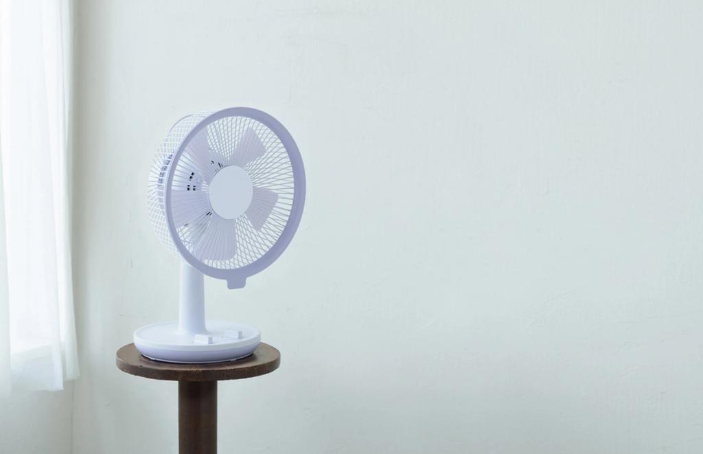 White desktop fan on a round wooden stool beside a wall