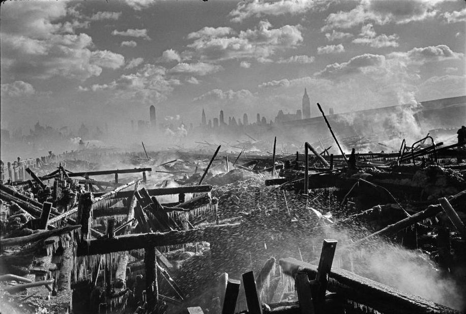 Smoking, ice-covered wooden wreckage against the silhouette of Manhattan skyscrapers