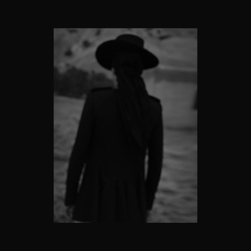 A dark silhouette of a person in a hat and coat, seen from behind, against a landscape