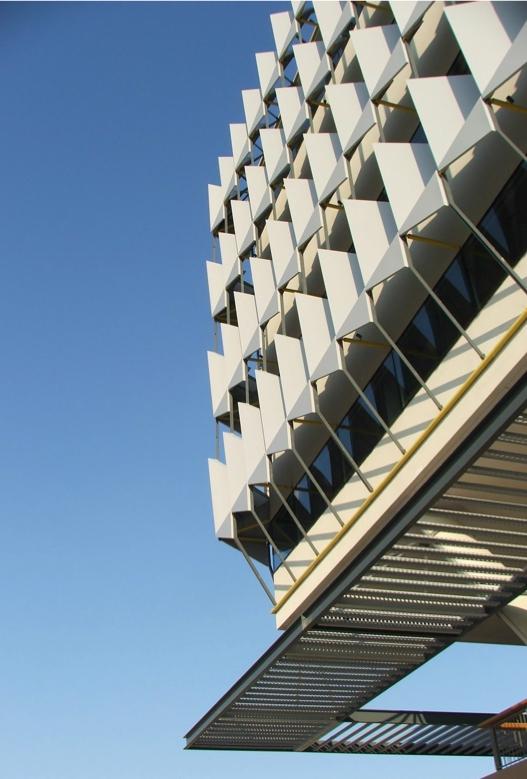 A low-angle view of a Masdar City building facade with rows of white, angled solar shading panels