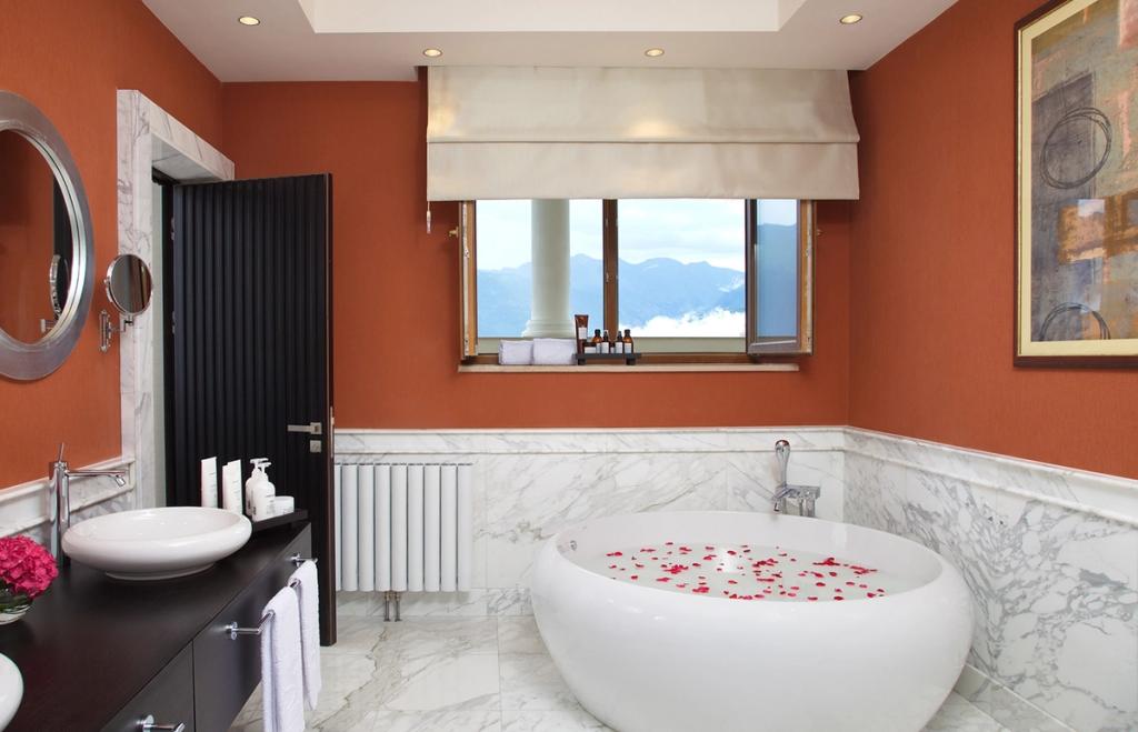 A bathroom with a round bathtub, rose petals, and a window overlooking the mountains of Krasnaya Polyana
