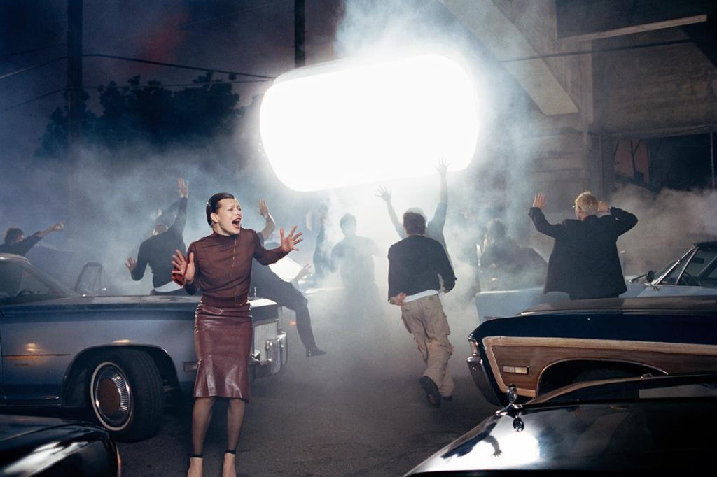 A screaming model in a leather dress amid smoke and old cars at night