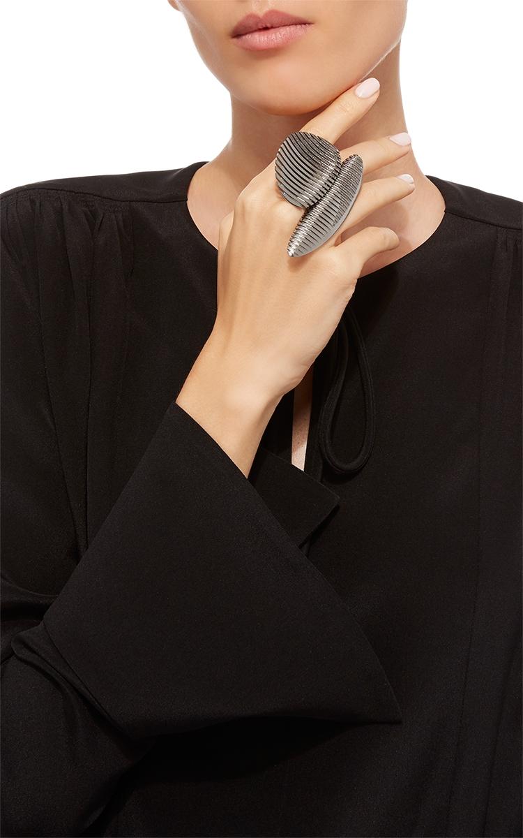 A dark grey ridged ring with a curved form on the hand of a model in a black dress