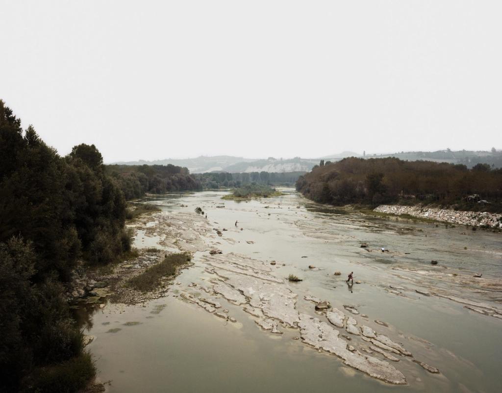 A shallow river with stony shallows and solitary fishermen, hills hazy on the horizon
