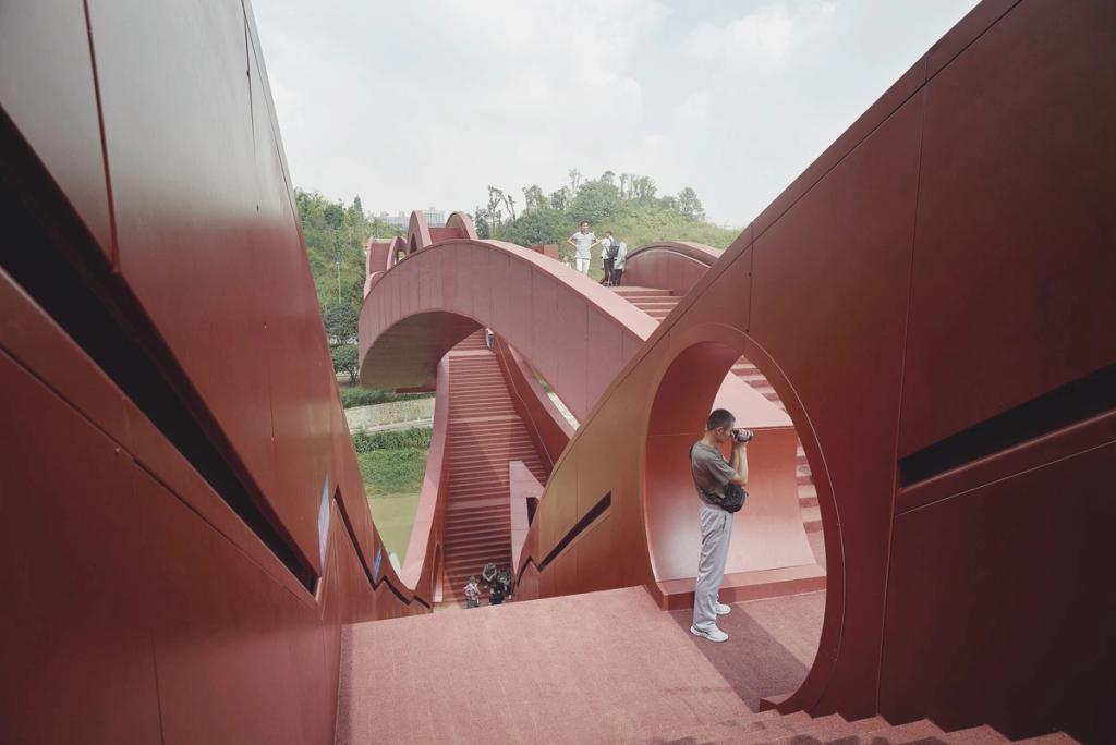 The red Lucky Knot Bridge in China: a close-up of the interlocking loop pathways, with a man taking a photograph