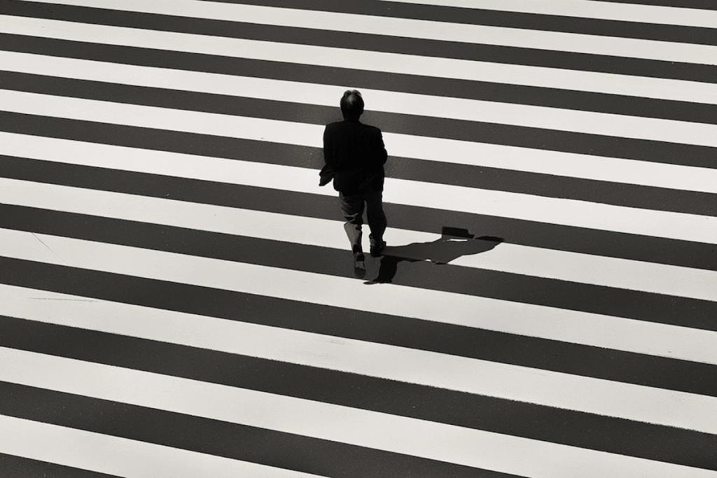 The silhouette of a person on a pedestrian crossing with black-and-white zebra stripes, seen from above