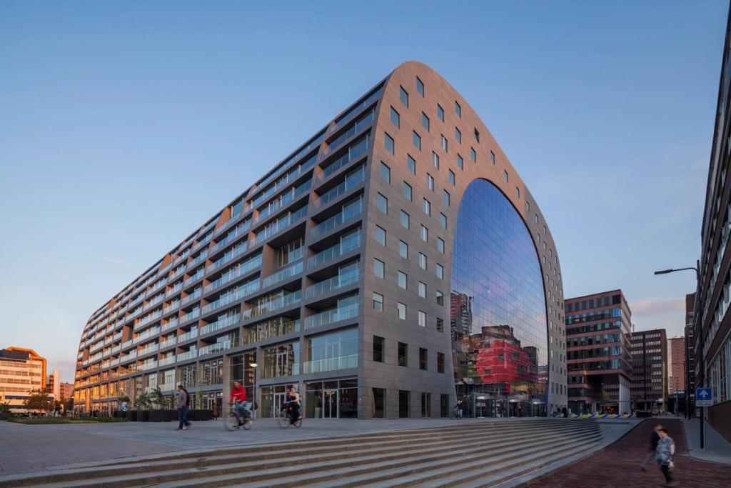 The residential stone facade of the Markthal, with a glazed arched end wall and a square in front of the entrance