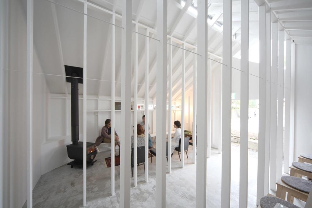 Белый интерьер Koyasan Guesthouse с гостями за столом и печью за вертикальными рейками