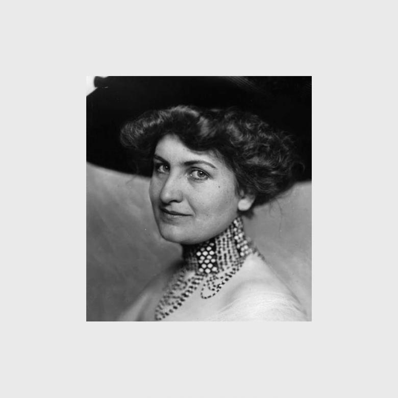 Black-and-white portrait of a woman with dark curly hair, wearing a hat and a pearl choker