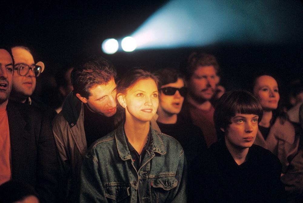 A crowd of young people watching a stage in the beam of spotlights, a girl in a denim jacket