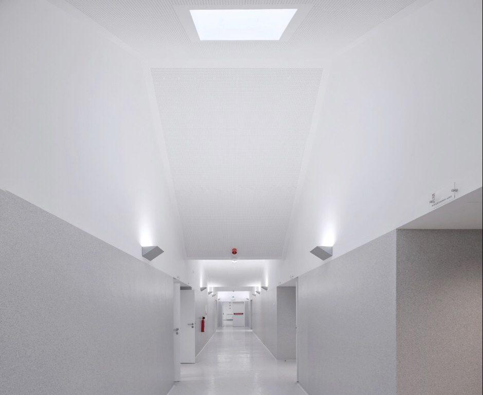The white minimalist corridor of Mouriz school with a slanted ceiling and overhead light