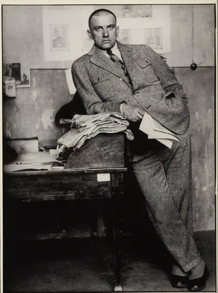 A portrait of Vladimir Mayakovsky in a suit, leaning against a writing desk