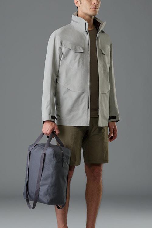 Мужчина в серой куртке-филд с серой сумкой в руке и хаки-шортах от Arc'teryx Veilance