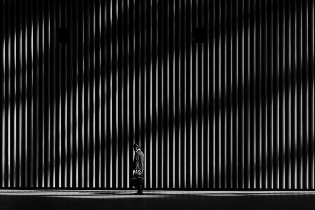 The silhouette of a person beside a tall wall of vertical fins with two circular openings