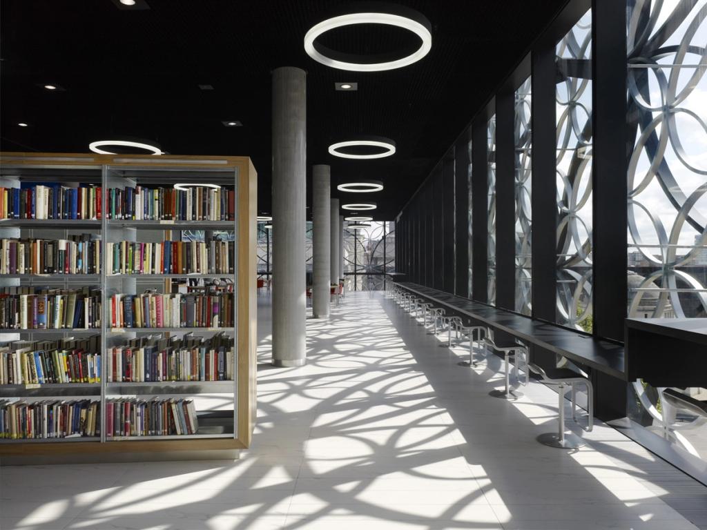 A bright hall in the Library of Birmingham with book stacks and a patterned facade casting shadows across the floor