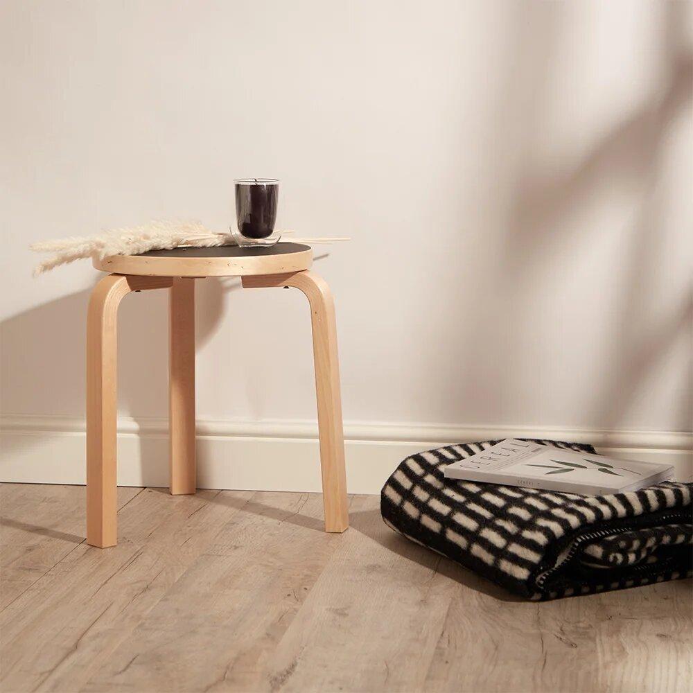 Alvar Aalto's Stool 60 on three bent birch legs, styled in an interior with a throw and a book