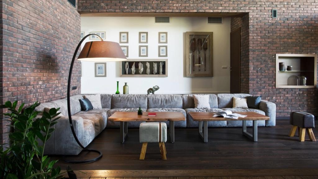Living room with brick walls, a grey corner sofa, a floor lamp and low wooden coffee tables