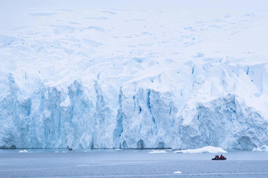 Inflatable boats carrying tourists alongside the sheer wall of a glacier at sea