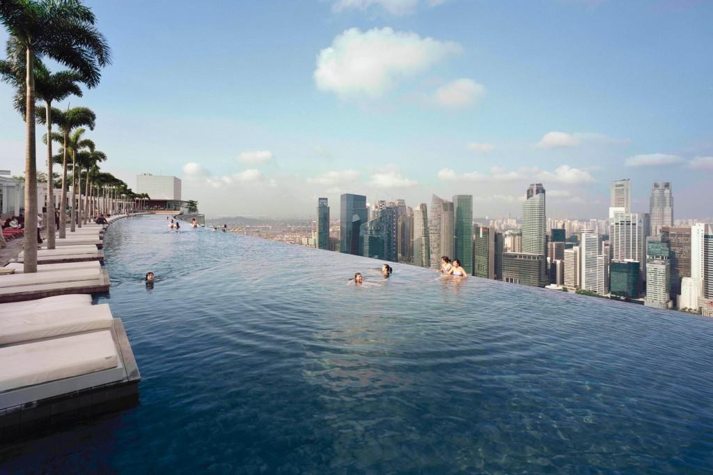 Люди в бесконечном бассейне Marina Bay Sands над небоскрёбами Сингапура