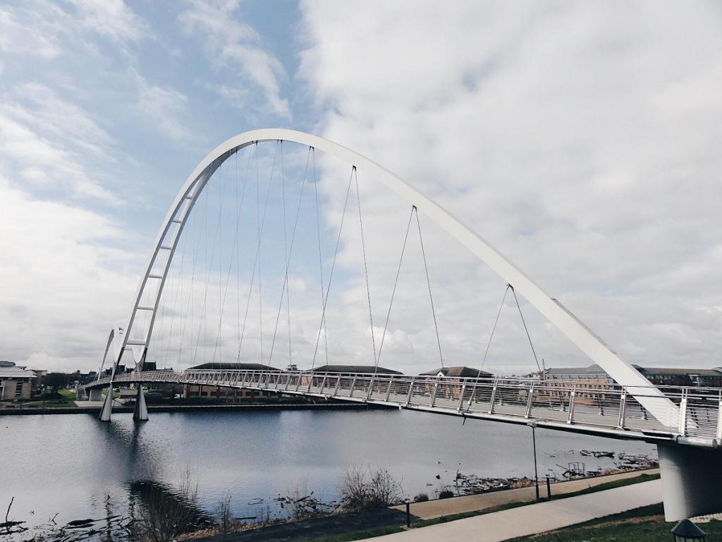 The Infinity Bridge by day: large and small white arches spanning a body of water beneath a cloudy sky