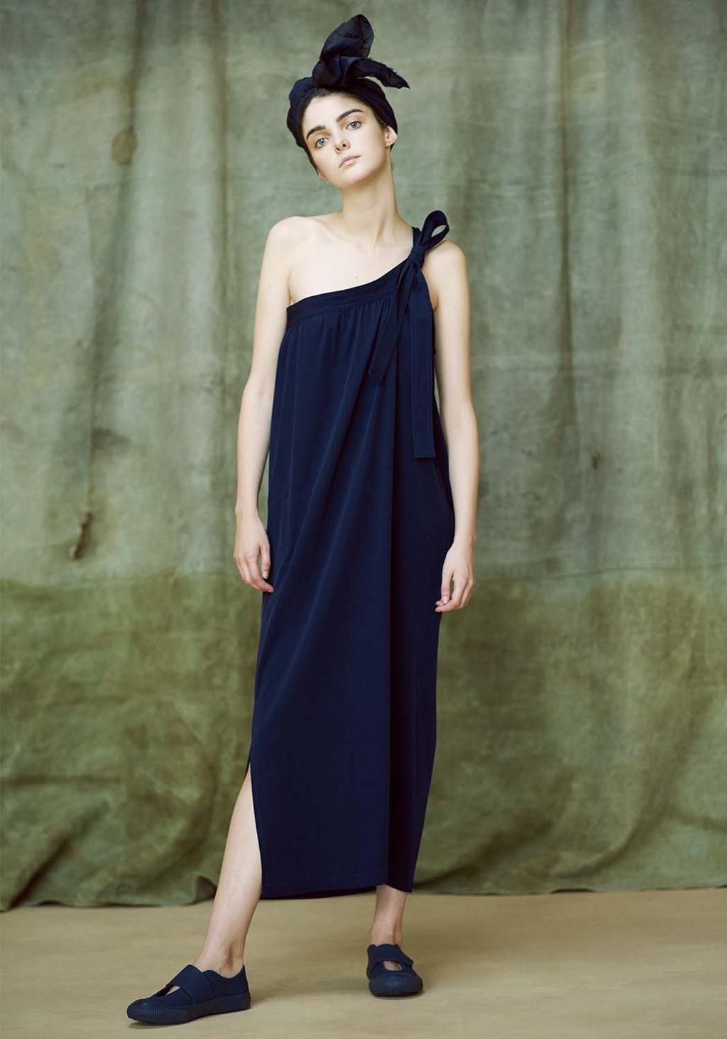 A model in a dark navy one-shoulder dress with a tie and a turban