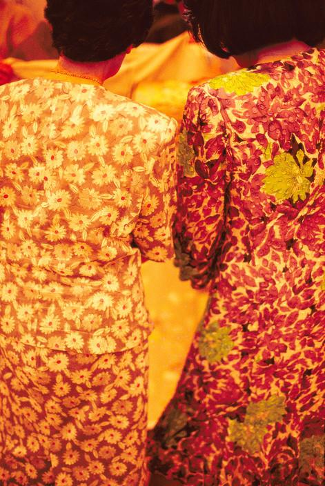 Two women seen from behind in floral dresses in warm golden-red light