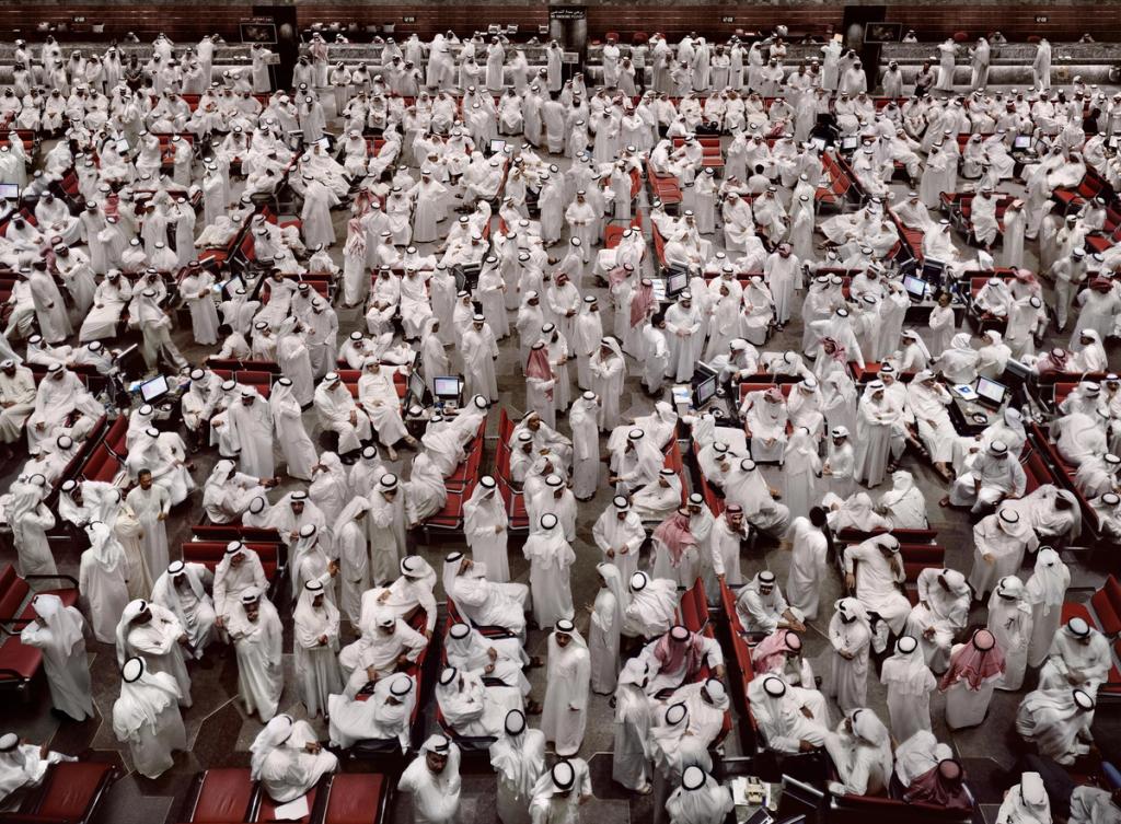 A stock-exchange floor densely packed with hundreds of people in white Arab dress