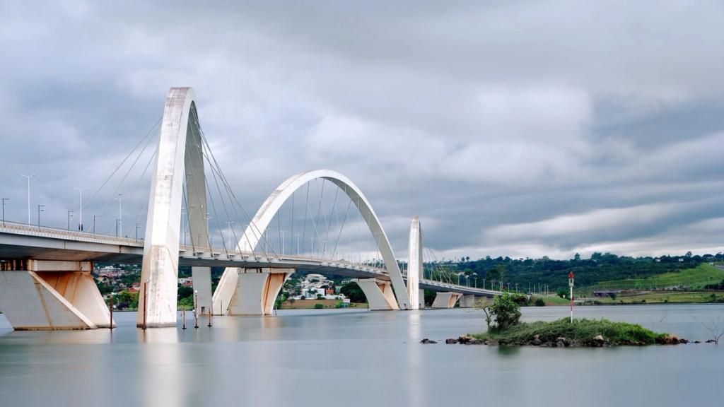 The three diagonal arches of the Juscelino Kubitschek Bridge over calm water beneath a cloudy sky