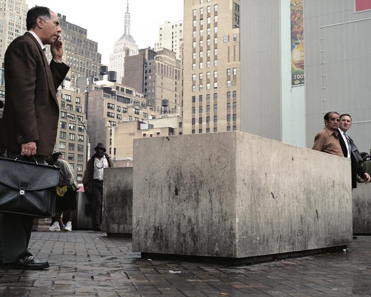 A man with a briefcase talking on the phone beside concrete blocks, with New York skyscrapers in the background