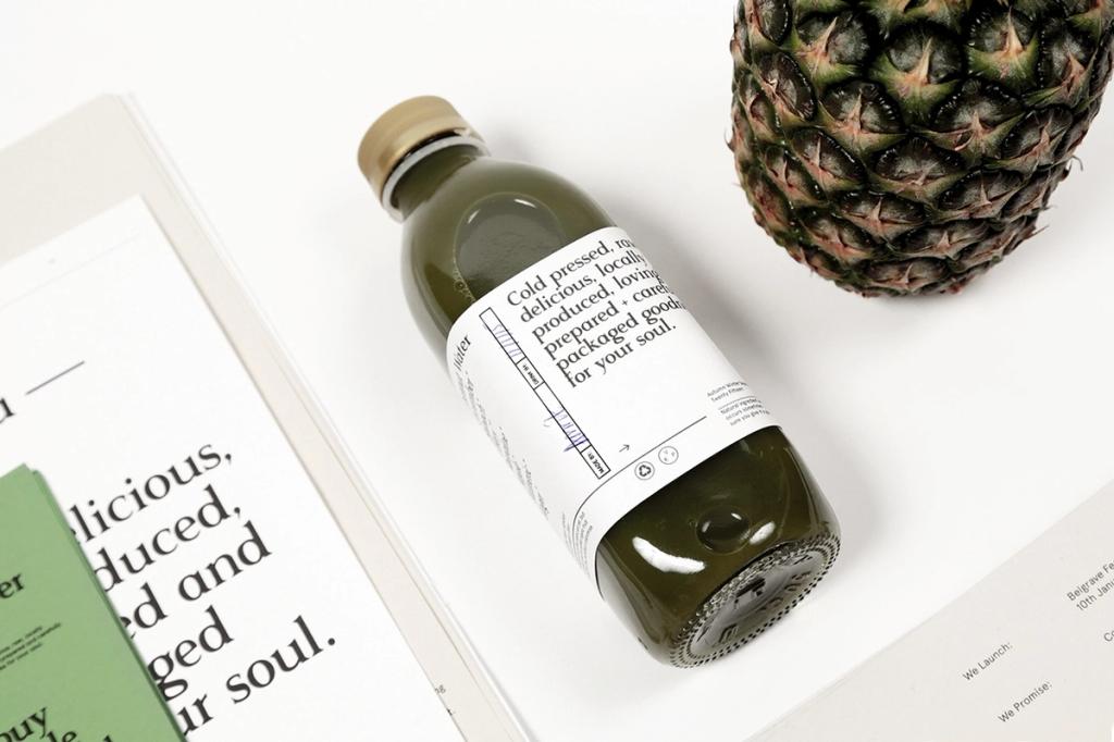 Лежащая зелёная бутылка сока Leeds Juicery рядом с ананасом на брошюре