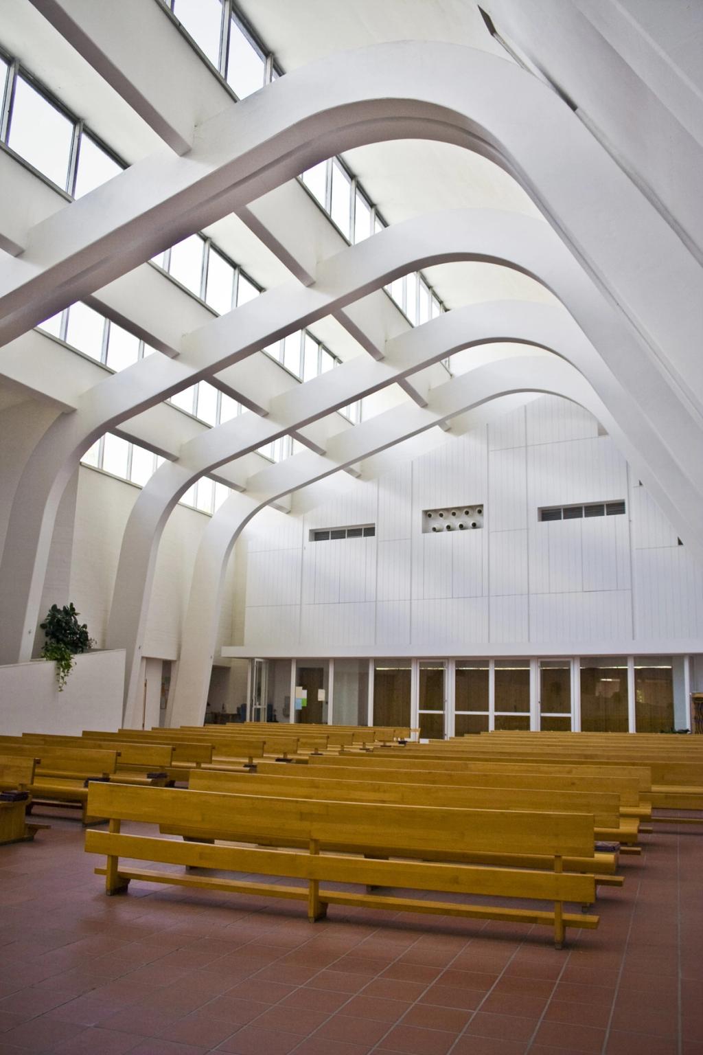 The nave of Riola Church, with a fan of white ribbed arches, overhead clerestory glazing and rows of pews
