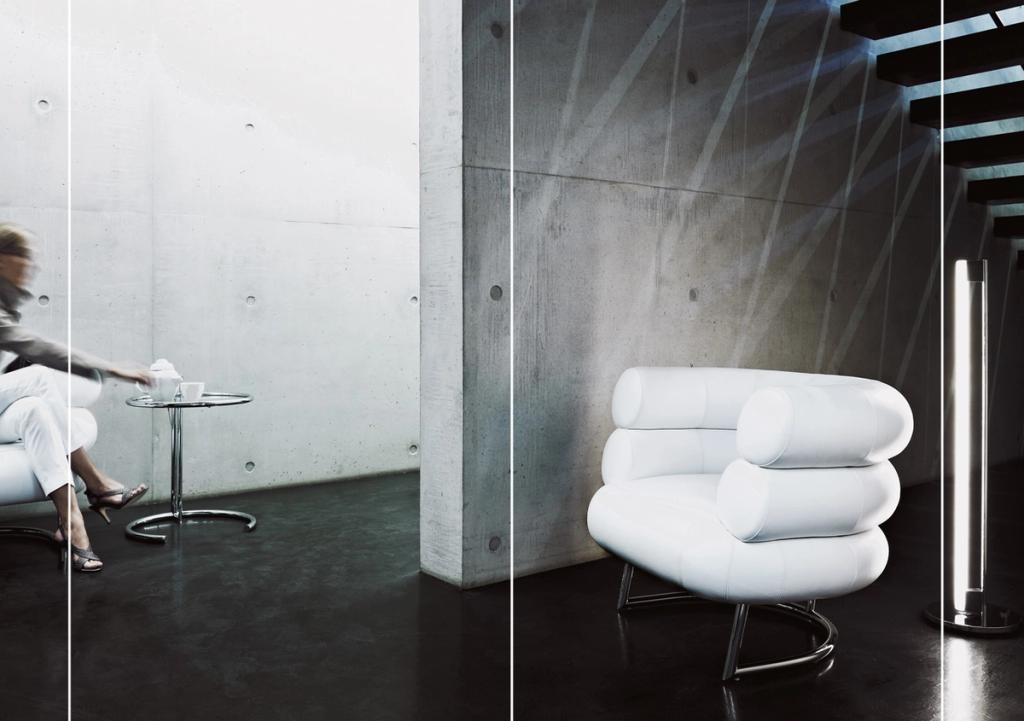 A white Bibendum armchair made of leather bolsters on a chromed base, against a concrete wall