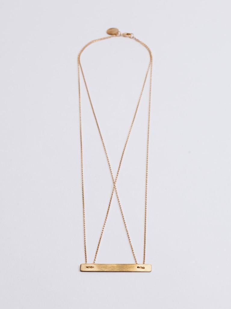A long gold Tribe Alive necklace with a horizontal bar pendant against a white background