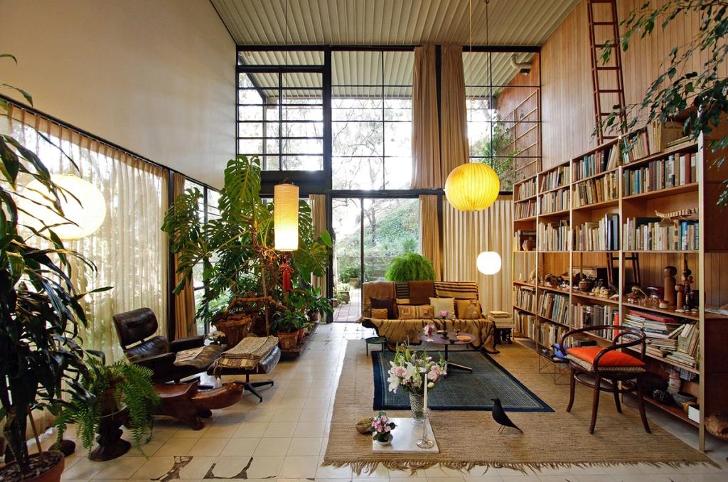 The interior of the Eames House with bookshelves, an armchair and an abundance of plants