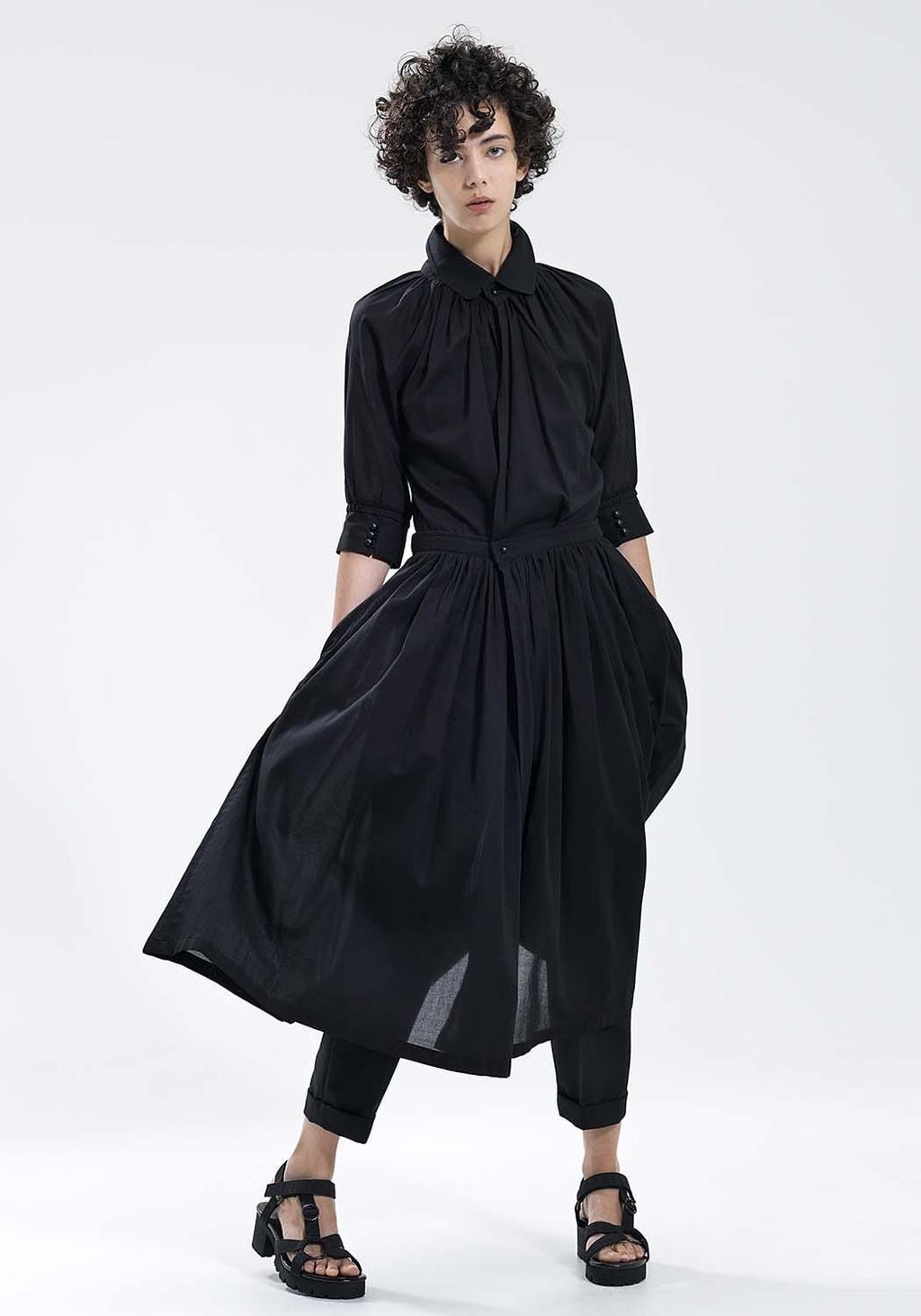 A model in a black gathered shirt-dress worn over tapered trousers